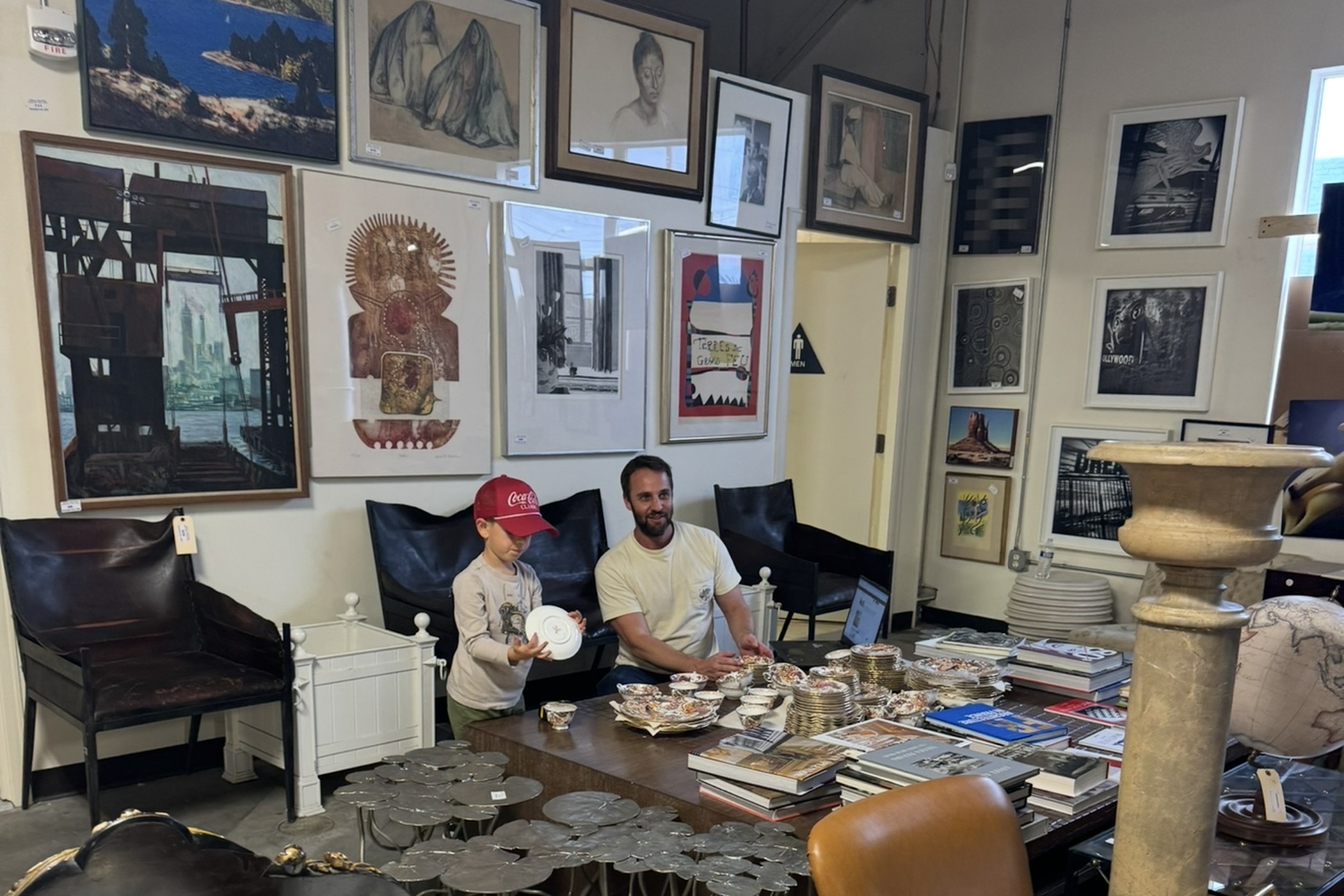 Two generations of the Abell family laying out a porcelain service on a table in the gallery, a wall of catalogued pictures behind them