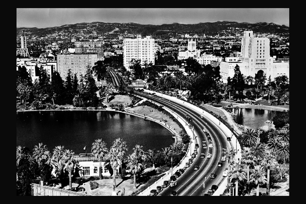Wilshire Boulevard curving past the lake at MacArthur Park, Los Angeles, with the towers of the Westlake district beyond