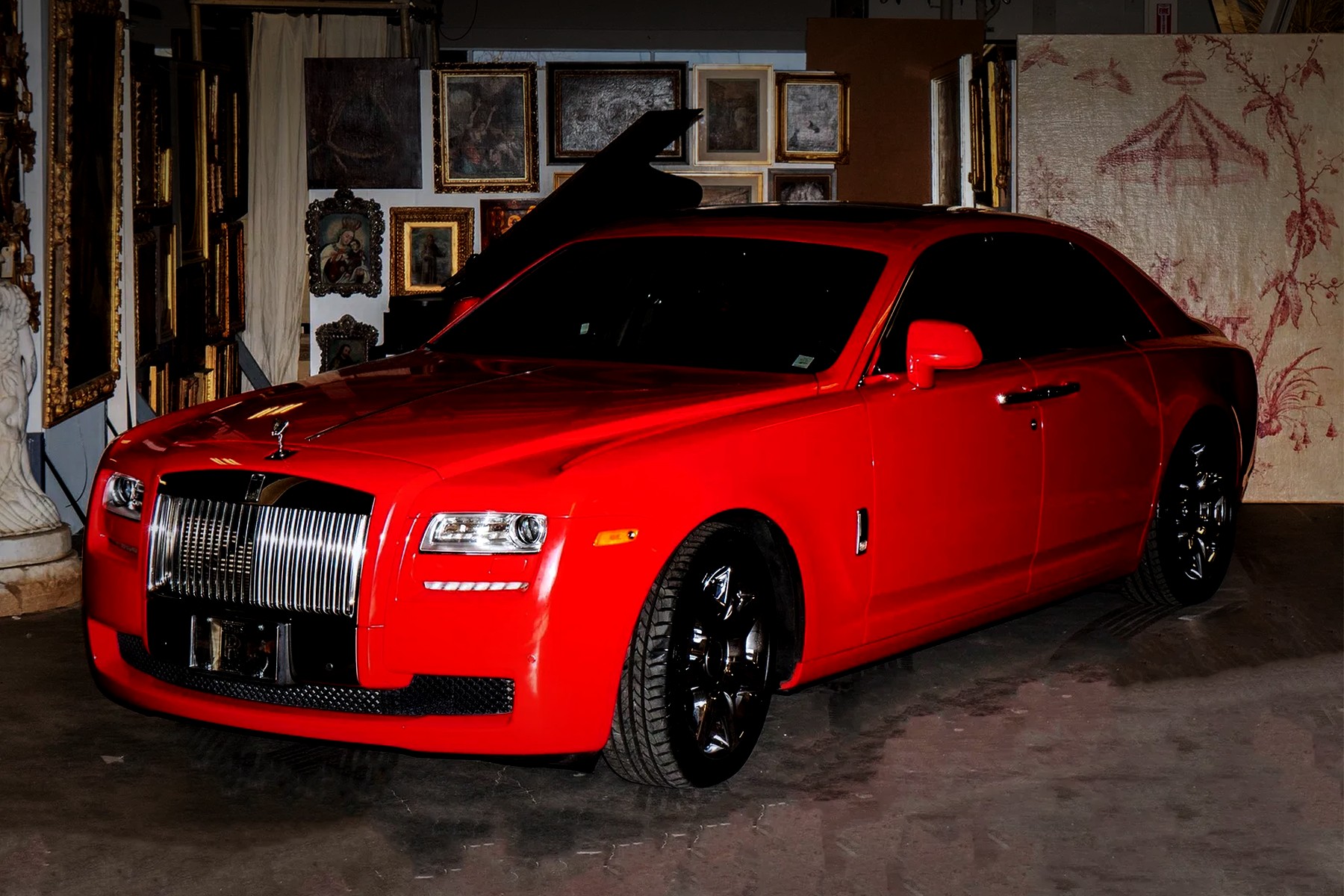 A red Rolls-Royce Ghost in the Abell warehouse among paintings, frames and a grand piano