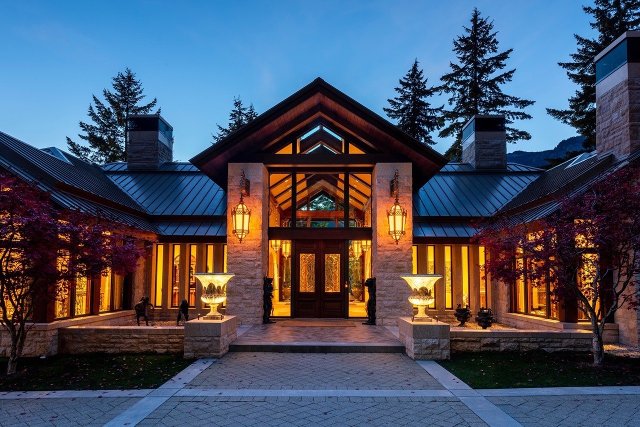 The lit stone-and-timber entrance of a lakefront house in Whistler, British Columbia, photographed at dusk
